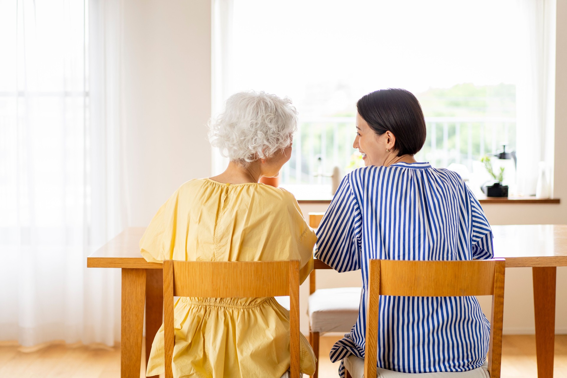 Two Asian women are sitting on chairs and talking.
